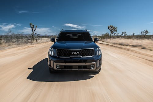 Free Front view of an SUV driving fast on a desert dirt road under a clear blue sky. Stock Photo